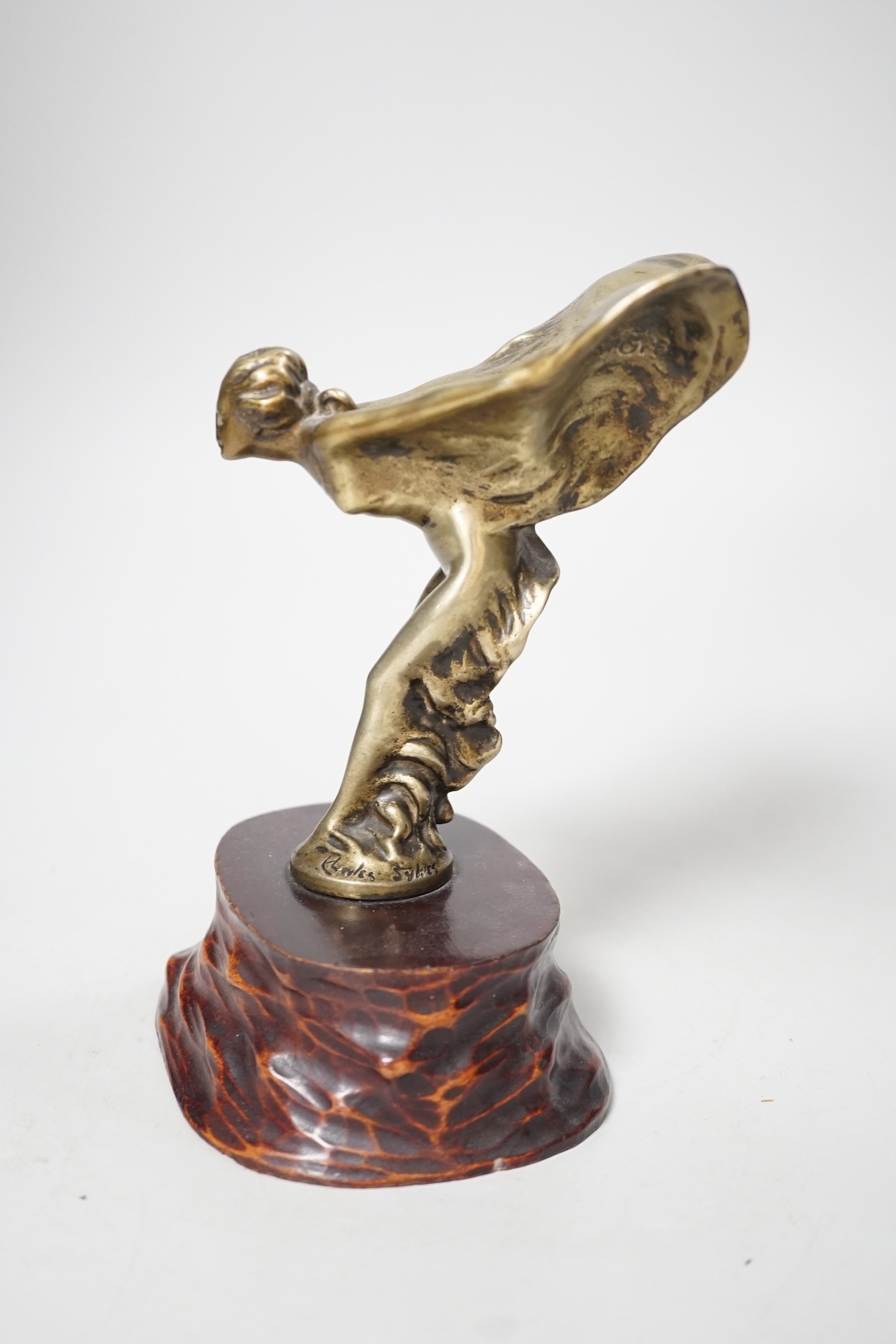 After Charles Sykes, a gilt metal Rolls Royce car mascot - ‘’Spirit of Ecstasy’’, inscribed and bearing date 1911, on a carved wooden plinth. 17.5cm tall